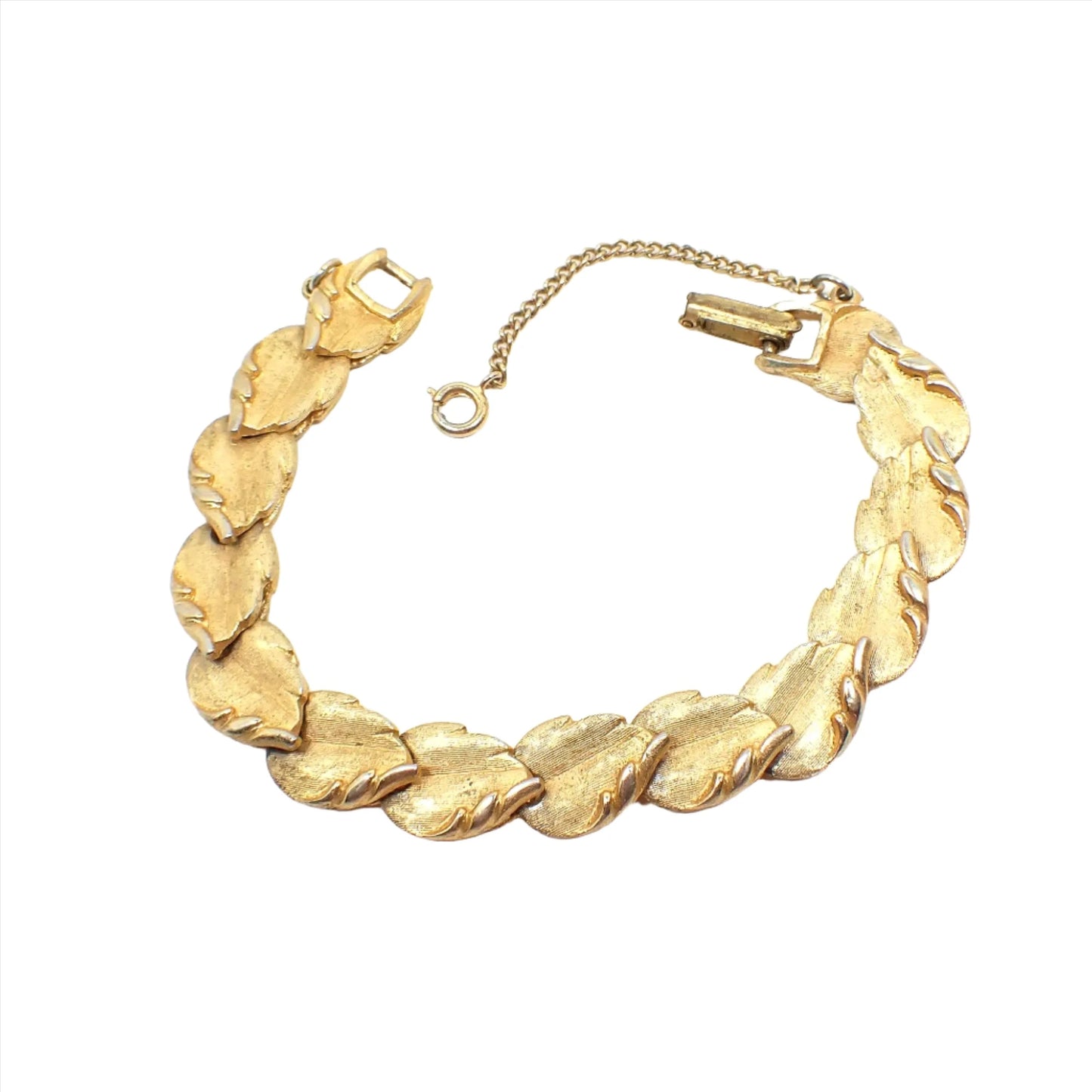 Top view of the Mid Century vintage link bracelet. The metal is textured and gold tone in color. Each link is shaped like a leaf with a curled edge. There is a snap lock clasp and safety chain at the end. 