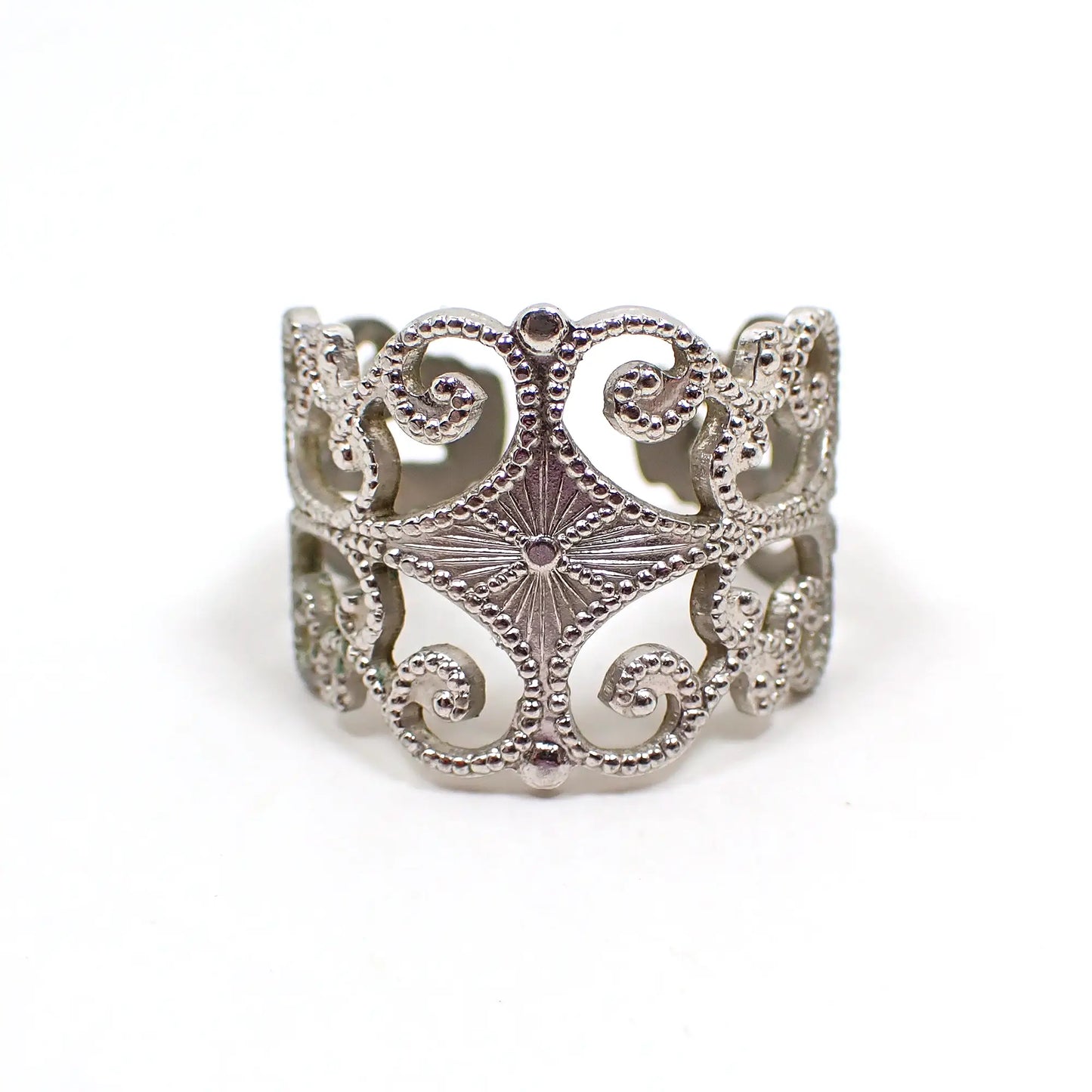 Front view of the retro vintage Sarah Coventry adjustable ring. The metal is silver tone in color. It has a filigree pattern with dots on curls and a diamond shaped area on the middle front with a starburst design.