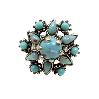 Front view of the retro vintage adjustable ring. It has a floral design with round and teardrop shaped fancy glass cabs in an aqua blue color. Some of the cabs also have spots of red and white color. The metal is silver tone in color.