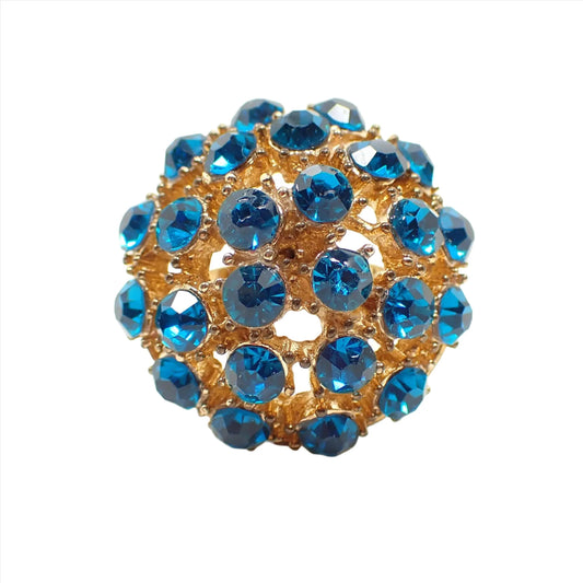 Front view of the Mid Century vintage adjustable ring. The metal is gold tone in color. The top is domed and round with filigree openings. There are round bright teal blue rhinestones with small balls of metal in between them for a brutalist style look.