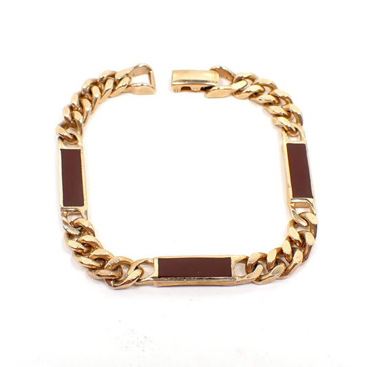 Top view of the retro vintage Avon enameled link chain bracelet. The metal is gold tone in color. There are three rectangle bar links that are burgundy colored enameled in between wider curb chain. There is a snap lock clasp at the end.