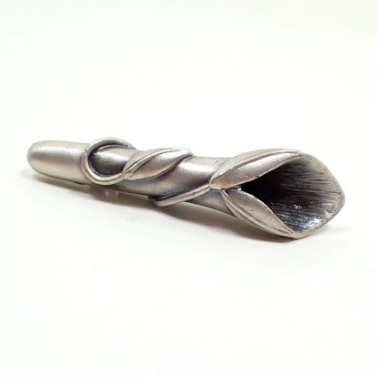 Angled view of the retro vintage pewter boutonniere brooch pin. The metal is light pewter gray in color. It is shaped like a tube with a steam and leaves wrapped around it. There is a flared opening at the top to put the small flowers into.