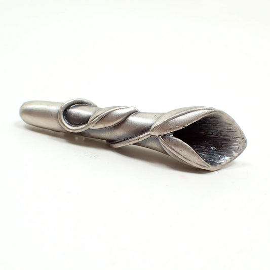 Angled view of the retro vintage pewter boutonniere brooch pin. The metal is light pewter gray in color. It is shaped like a tube with a steam and leaves wrapped around it. There is a flared opening at the top to put the small flowers into.