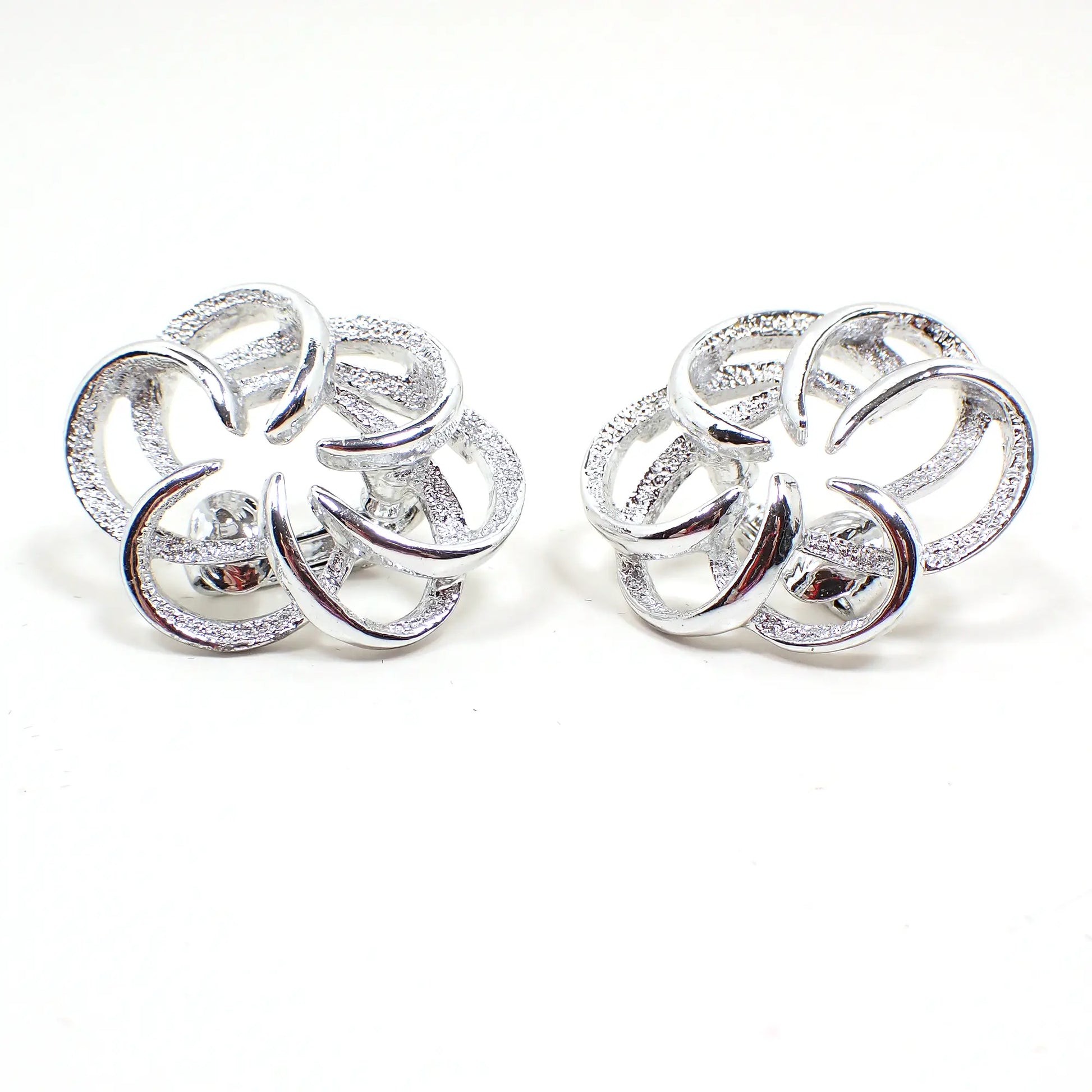 Front view of the Mid Century vintage Sarah Coventry Tailored Swirl earrings. The metal is silver tone in color. They are shaped like a swirled pinwheel with open textured matte and shiny areas.