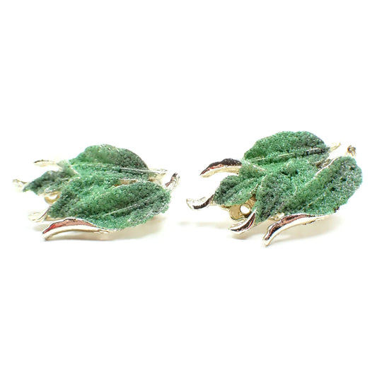 Front view of the Mid Century vintage sugar coated clip on earrings. The metal is gold tone in color and they are shaped like leaves. There are tiny little round green glass beads across the surface of the earrings.