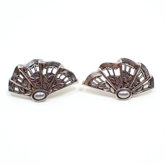 Front view of the retro vintage clip on earrings. The earrings were photographed sideways. They have a ruffled filigree fan design and a small very light gray faux pearl on the side. The metal is antiqued silver in color.