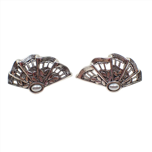 Front view of the retro vintage clip on earrings. The earrings were photographed sideways. They have a ruffled filigree fan design and a small very light gray faux pearl on the side. The metal is antiqued silver in color.
