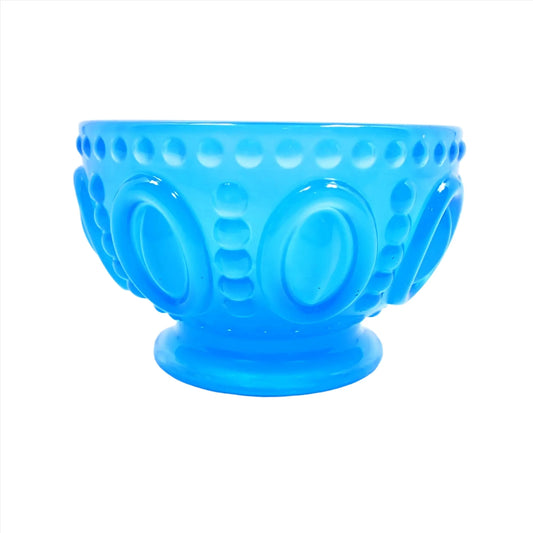 Side view of the small handmade resin decorative footed bowl. The resin is neon blue in color. The bowl has an oval design around the middle of it with rows of dots in between and around the top edge of the bowl.