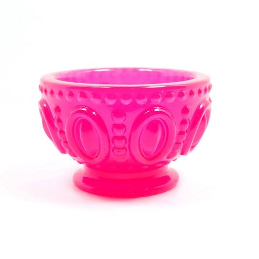 Side view of the small handmade resin decorative footed bowl. The resin is bright neon pink in color. The bowl has an oval design around the middle of it with rows of dots in between and around the top edge of the bowl. 