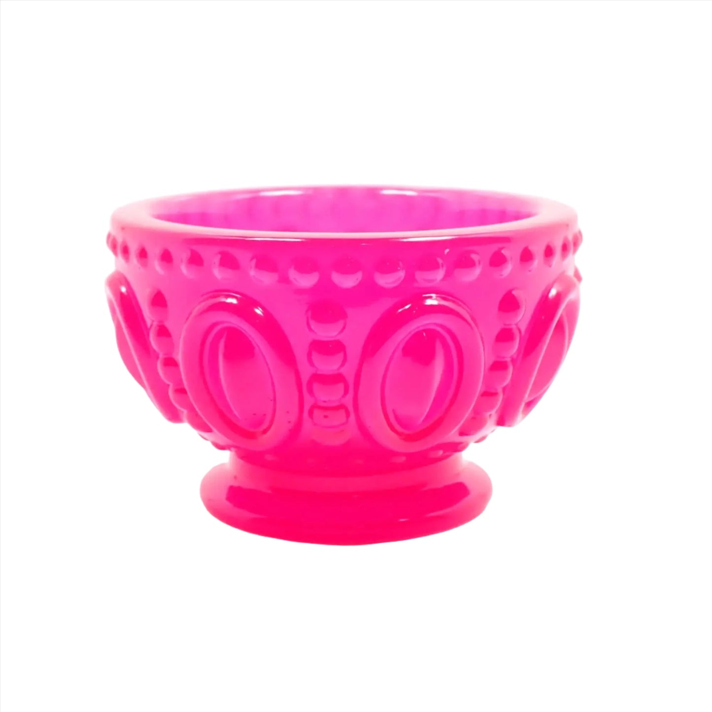 Side view of the small handmade resin decorative footed bowl. The resin is bright neon pink in color. The bowl has an oval design around the middle of it with rows of dots in between and around the top edge of the bowl. 