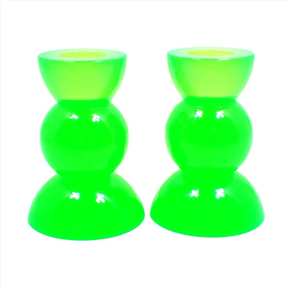 Side view of the handmade neon resin rounded geometric candlestick holders. They are neon green in color. They are shaped with a semi circle at the top and bottom with a sphere shape in between.