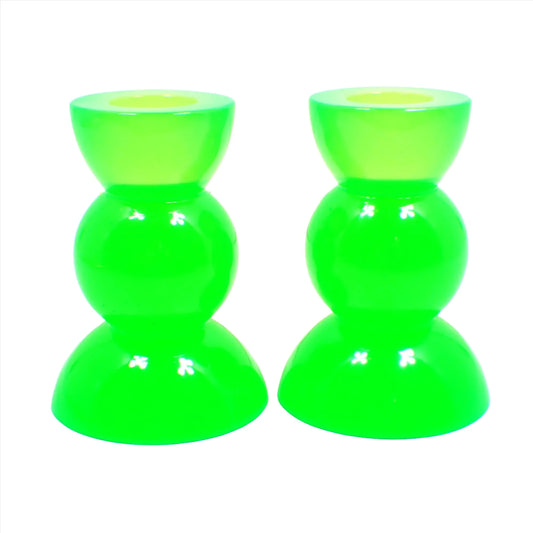 Side view of the handmade neon resin rounded geometric candlestick holders. They are neon green in color. They are shaped with a semi circle at the top and bottom with a sphere shape in between.