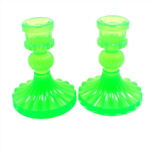 Side view of the vintage style handmade resin candlestick holders. They have a round cylinder style shape at the top, a corrugated round middle, and a flared out bottom with a corrugated ripple design. The resin is semi translucent neon green.