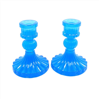 Side view of the vintage style handmade resin candlestick holders. They have a round cylinder style shape at the top, a corrugated round middle, and a flared out bottom with a corrugated ripple design. The resin is semi translucent neon blue.
