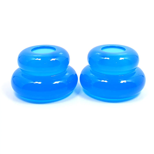 Side view of the pair of handmade double ring candlestick holders. They are shaped like puffy donut rings with a larger one on bottom and a smaller one on top. The resin is neon blue in color. There is a round hole at the top for the candlesticks to go in.