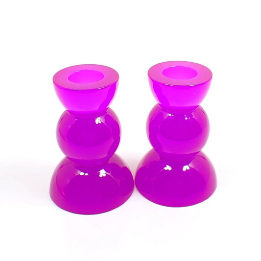 Side view of the handmade neon resin rounded geometric candlestick holders. They are neon purple in color. They are shaped with a semi circle at the top and bottom with a sphere shape in between.