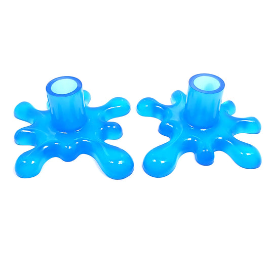Angled view of the handmade resin larger sized splat style candlestick holders. They are neon blue in color. The top part that holds the candle is round tube shaped. The bottom has a splat drip style design that is asymmetrical and has rounded ends.