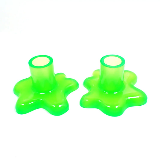 Photo of the handmade resin candlestick holders with splat design. The resin is semi translucent neon green in color. There is a cylindrical tube at the top part for the candlestick to go in and the bottom has an asymmetrical splat like design with rounded edges.