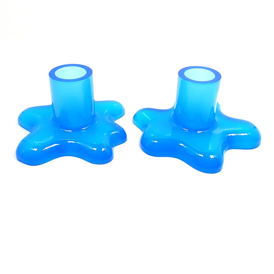 Photo of the handmade resin candlestick holders with splat design. The resin is semi translucent neon blue in color. There is a cylindrical tube at the top part for the candlestick to go in and the bottom has an asymmetrical splat like design with rounded edges.