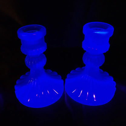 Photo showing the handmade vintage style neon blue resin candlestick holders fluorescing under a UV light in a deep blue color.