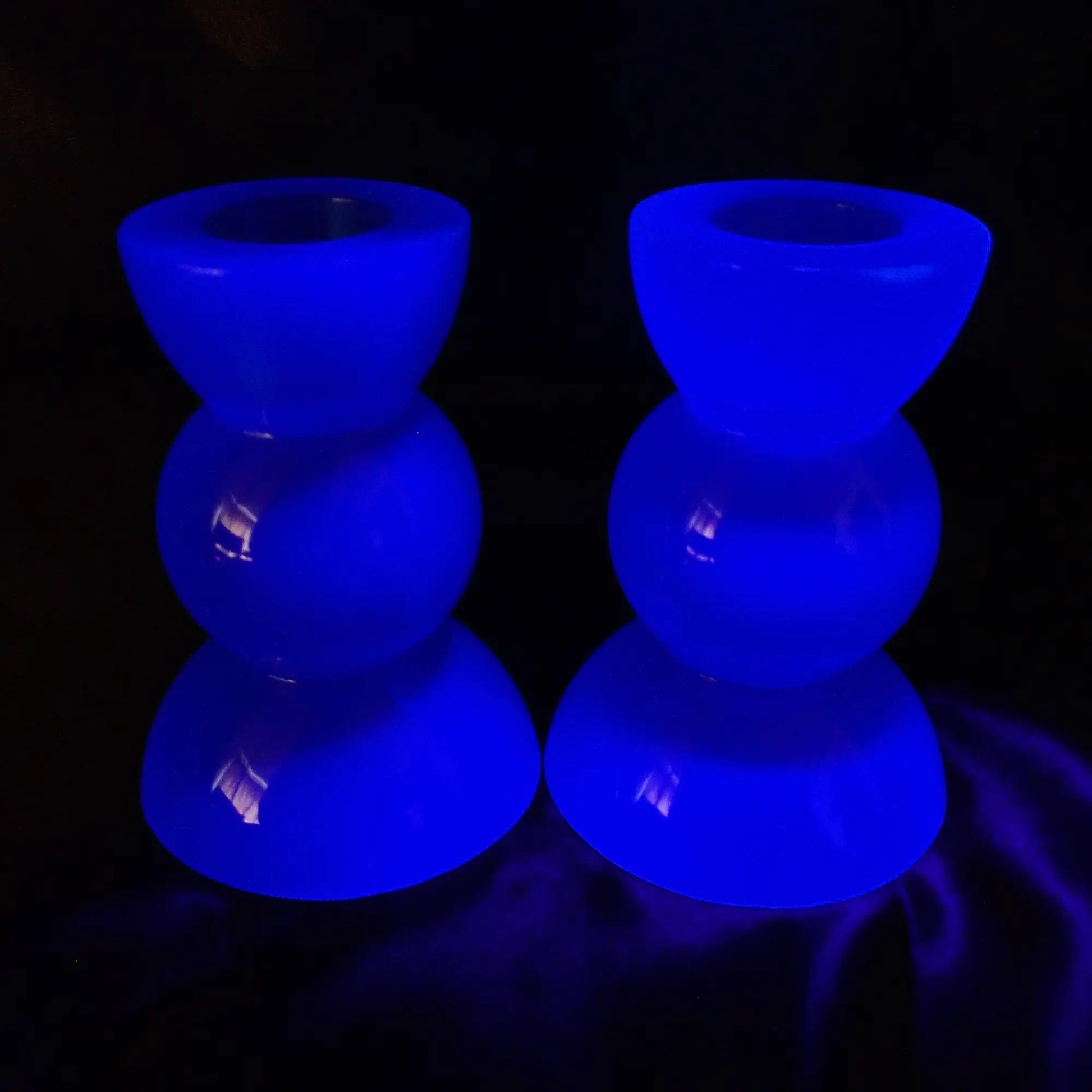 Photo showing the handmade neon blue resin candlestick holders fluorescing under a UV light.