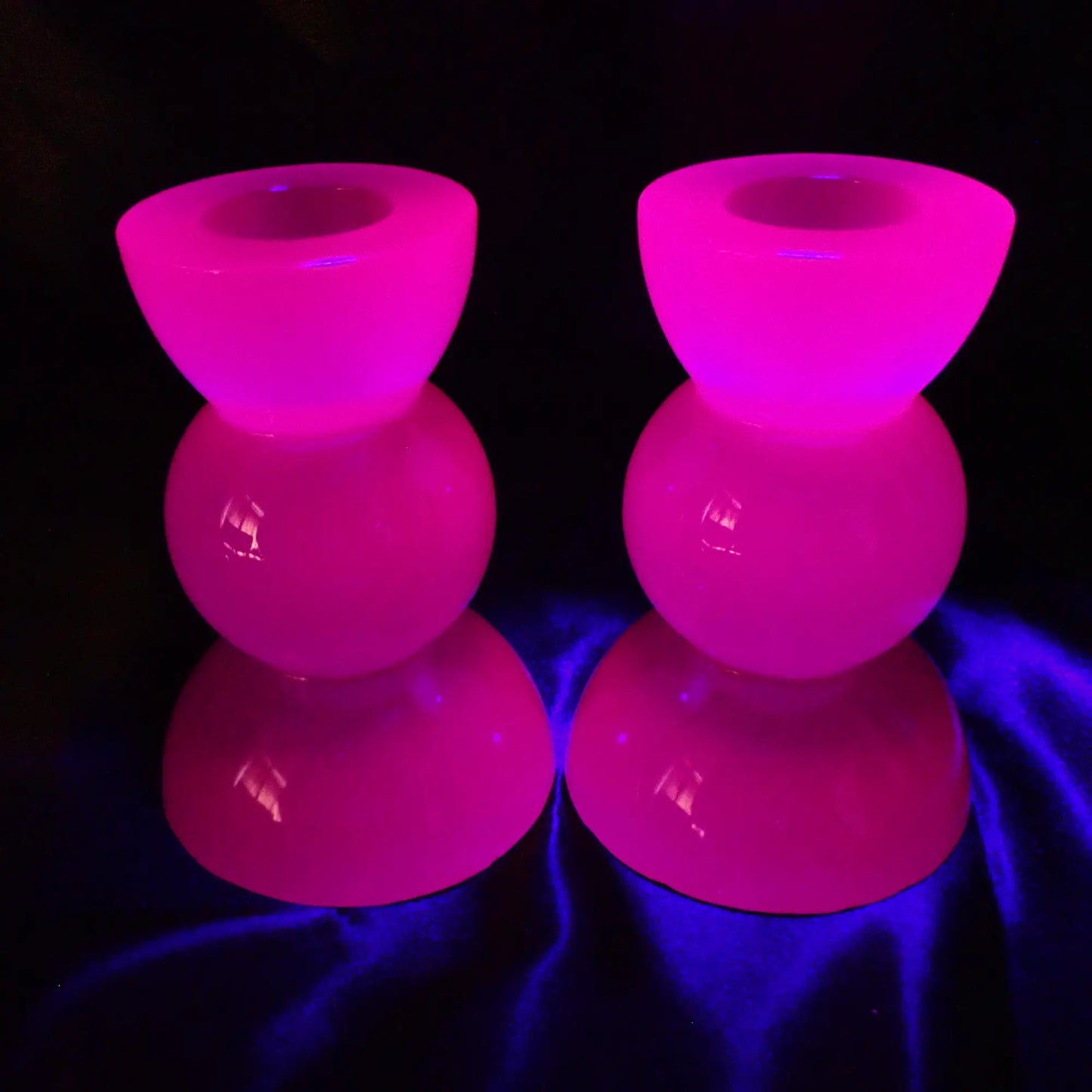 Photo showing the handmade neon purple resin candlestick holders fluorescing under a UV light in a pink color.