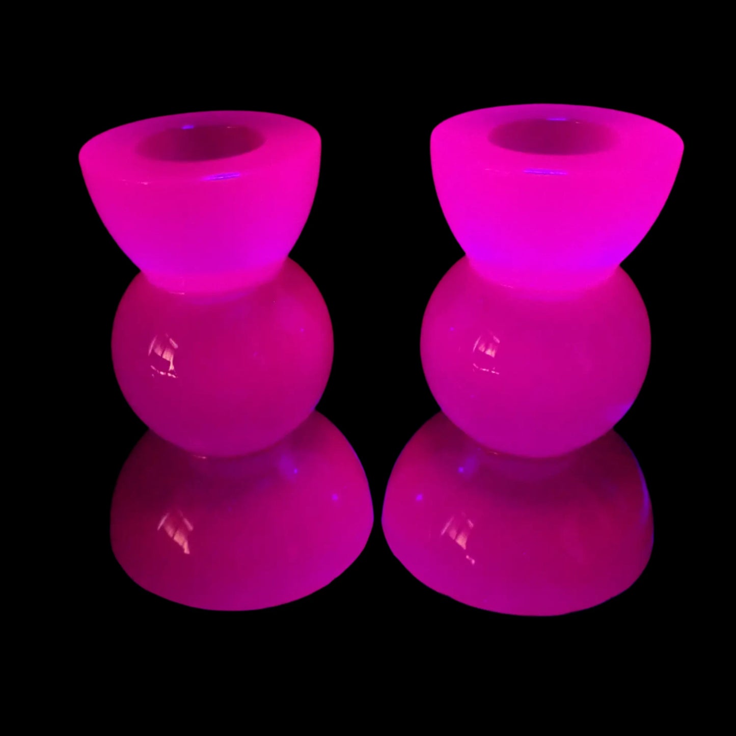 Photo showing the handmade neon purple resin candlestick holders fluorescing under a UV light in a pink color.