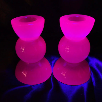 Photo showing the handmade neon purple resin candlestick holders fluorescing under a UV light in a pink color.