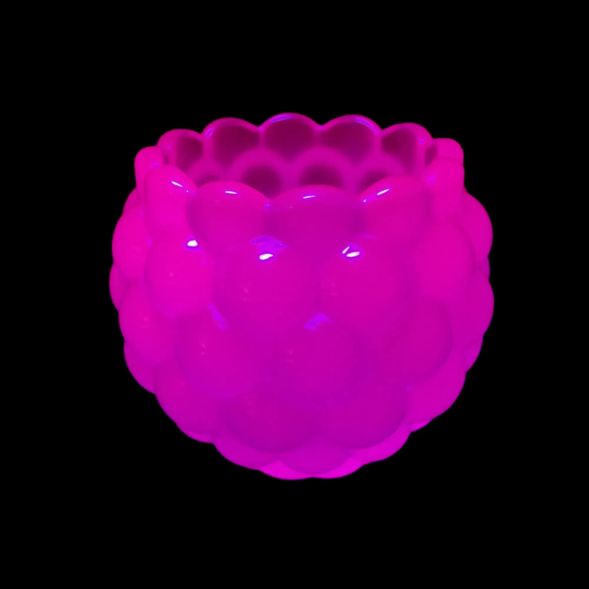 Photo showing how the Small Handmade Round Neon Purple Resin Pot with Scalloped Edge fluoresces under a UV light. It has a pink glow in color under UV.