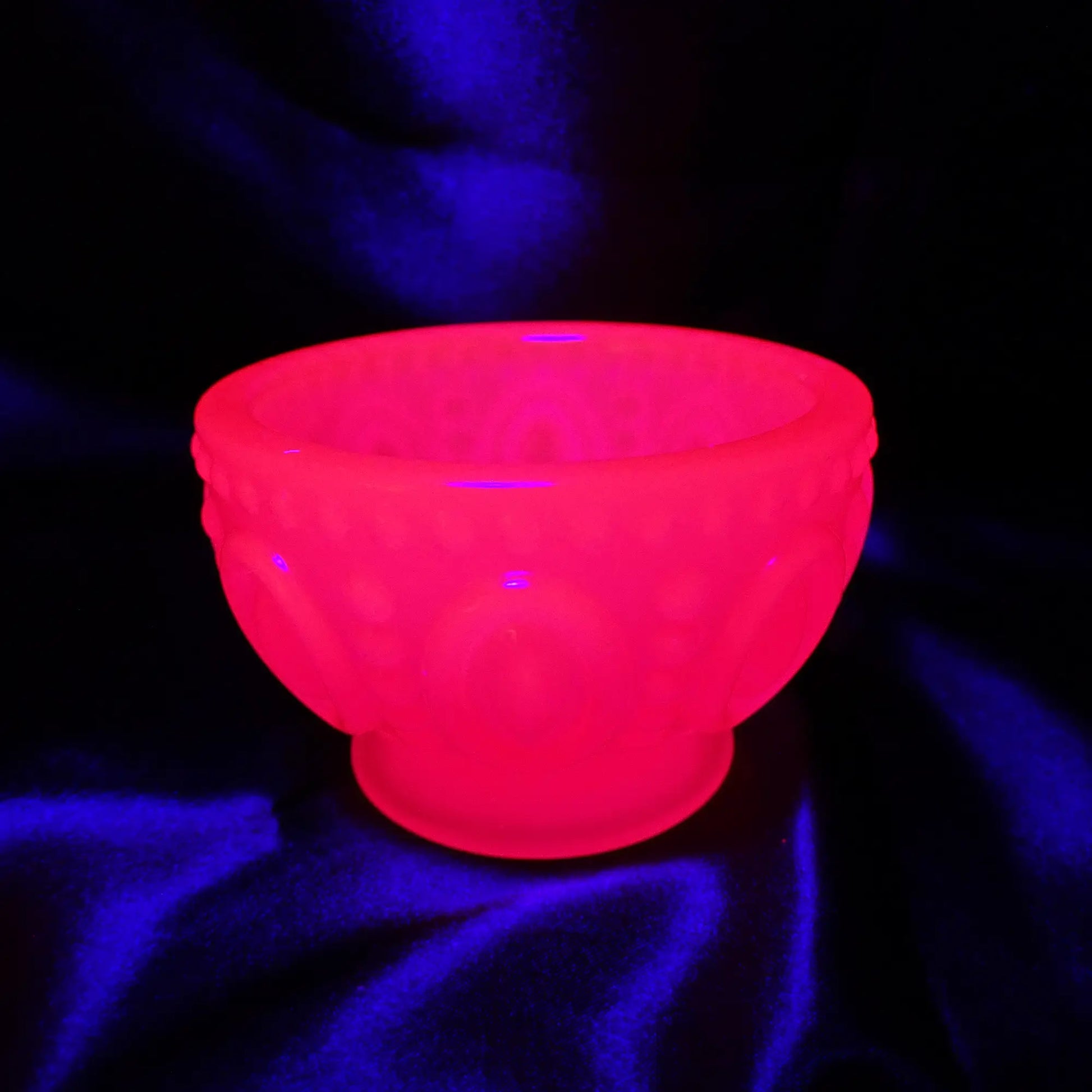 Photo showing how the Small Handmade Neon Pink Resin Decorative Footed Bowl with Oval and Dot Pattern fluoresces under a UV light.