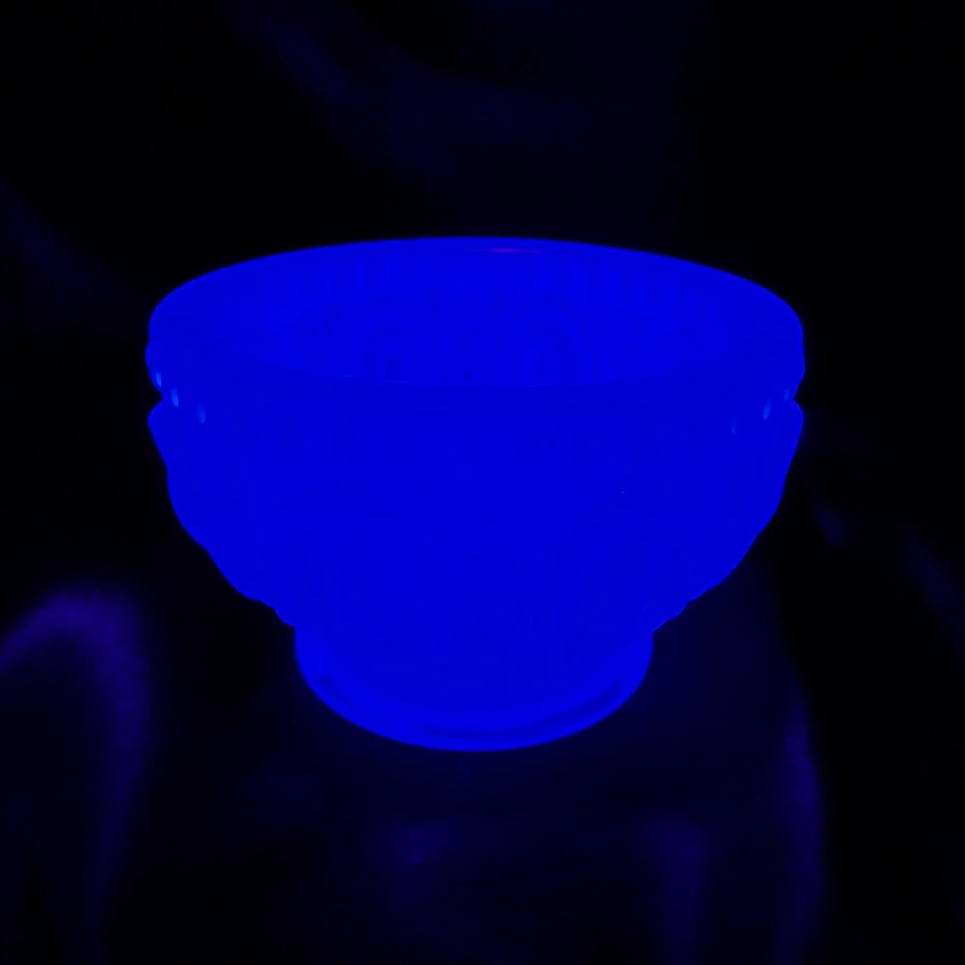 Photo showing how the Small Handmade Neon Blue Resin Decorative Footed Bowl with Oval and Dot Pattern fluoresces under a UV light.