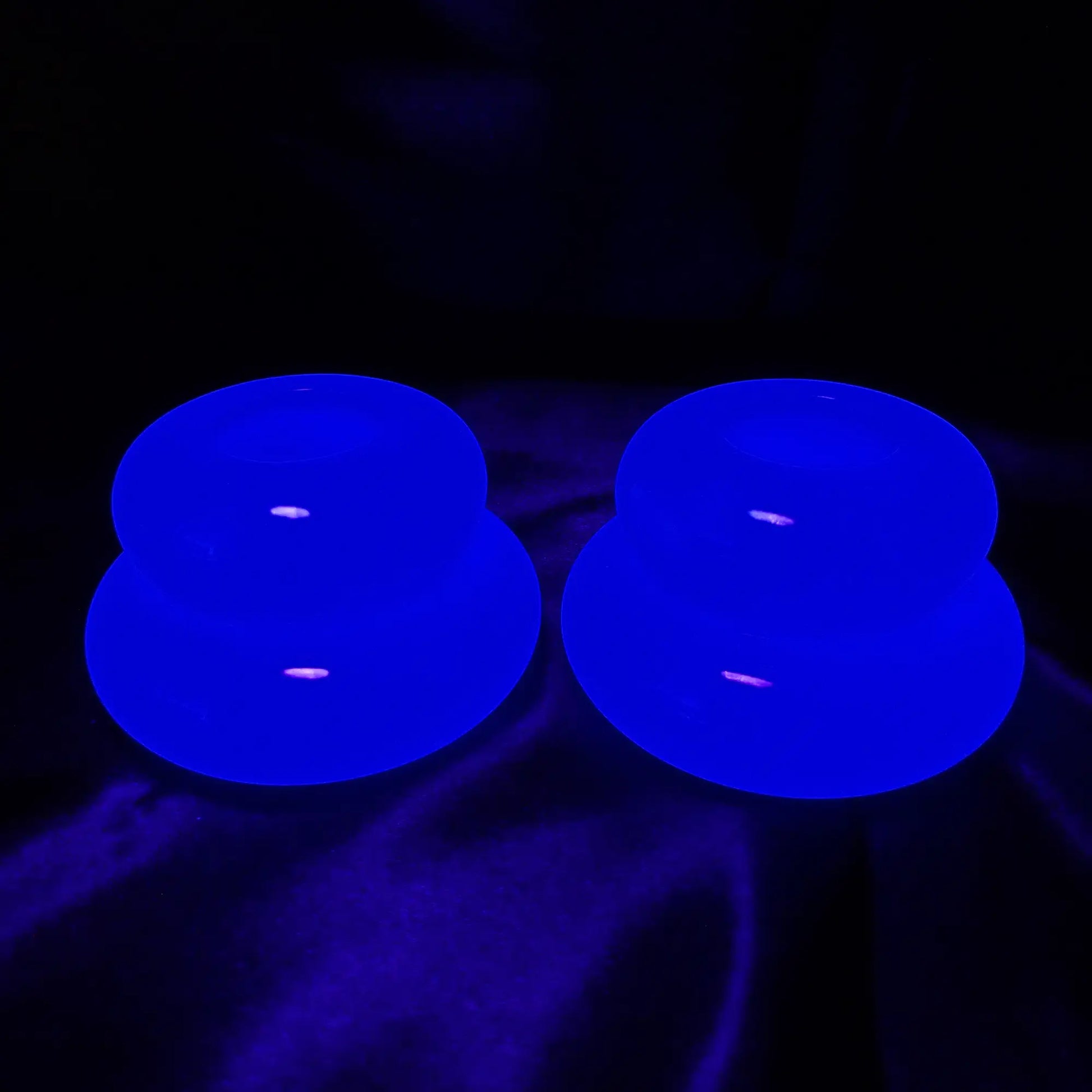 Photo showing the handmade neon blue resin candlestick holders fluorescing under a UV light.