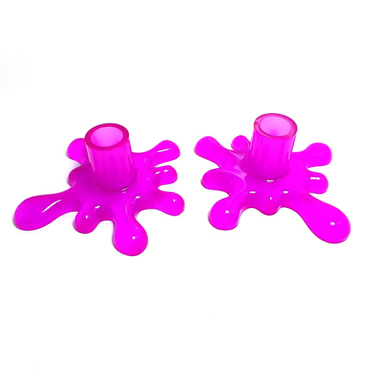 Angled view of the handmade resin larger sized splat style candlestick holders. They are neon purple in color. The top part that holds the candle is round tube shaped. The bottom has a splat drip style design that is asymmetrical and has rounded ends.