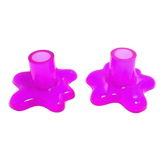 Photo of the handmade resin splat style candlestick holders. They are neon purple in color. The top part that holds the candle is round tube shaped. The bottom has a splat drip style design that is asymmetrical and has rounded ends.