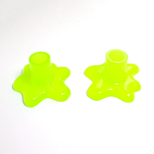 Photo of the handmade resin candlestick holders with splat design. The resin is semi translucent neon yellow in color with a bright green tint. There is a cylindrical tube at the top part for the candlestick to go in and the bottom has an asymmetrical splat like design with rounded edges.