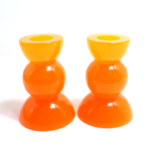 Side view of the handmade neon resin rounded geometric candlestick holders. They are neon orange in color. They are shaped with a semi circle at the top and bottom with a sphere shape in between.
