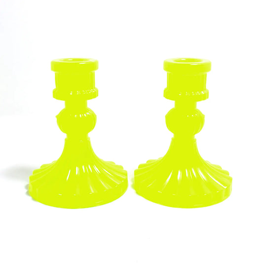 Side view of the vintage style handmade resin candlestick holders. They have a round cylinder style shape at the top, a corrugated round middle, and a flared out bottom with a corrugated ripple design. The resin is semi translucent bright neon yellow with a tint of bright green.