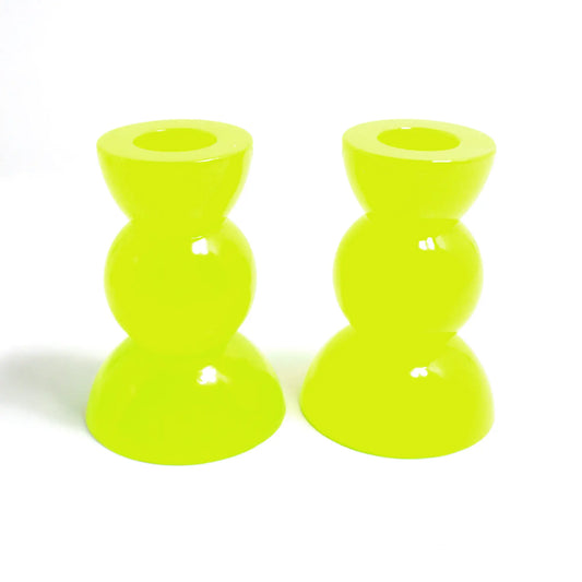 Side view of the handmade neon resin rounded geometric candlestick holders. They are bright neon yellow in color with a tint of bright green. They are shaped with a semi circle at the top and bottom with a sphere shape in between.