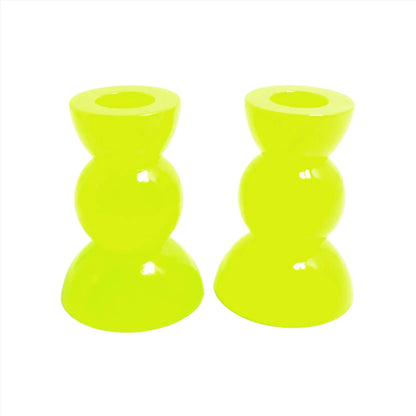Side view of the handmade neon resin rounded geometric candlestick holders. They are bright neon yellow in color with a tint of bright green. They are shaped with a semi circle at the top and bottom with a sphere shape in between.