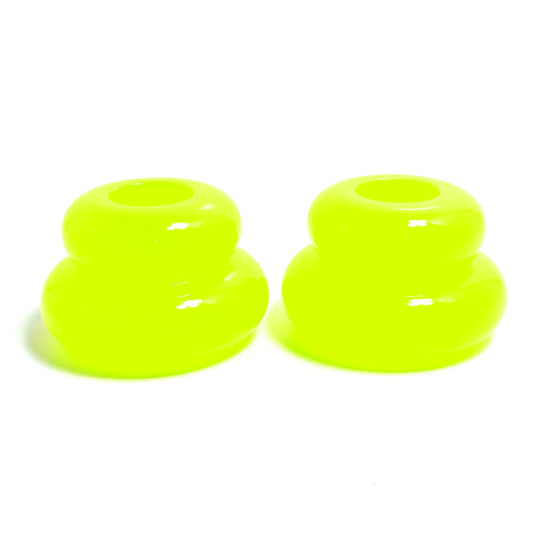 Side view of the pair of handmade double ring candlestick holders. They are shaped like puffy donut rings with a larger one on bottom and a smaller one on top. The resin is bright neon yellow in color with a tint of bright green. There is a round hole at the top for the candlesticks to go in.