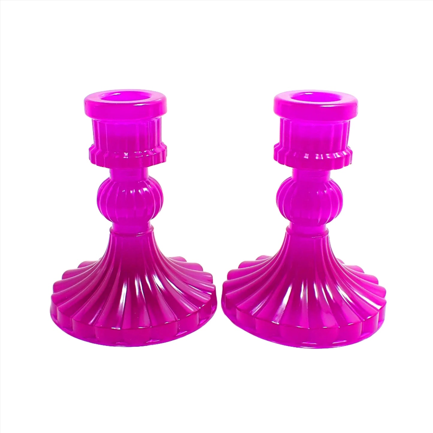 Side view of the vintage style handmade resin candlestick holders. They have a round cylinder style shape at the top, a corrugated round middle, and a flared out bottom with a corrugated ripple design. The resin is neon purple in color. 