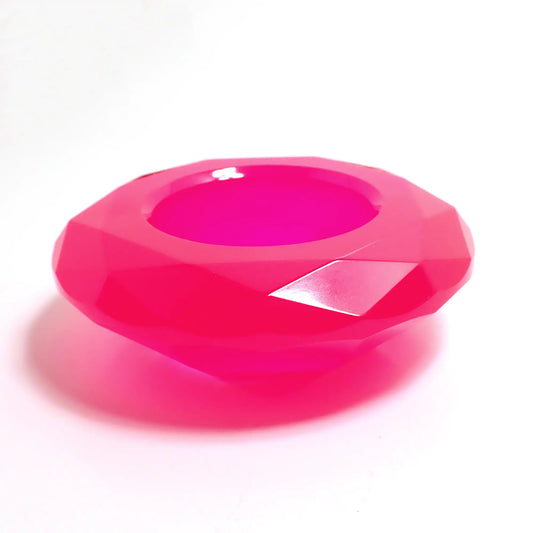 Photo of the handmade resin decorative pot. The resin is bright neon pink in color. It has a faceted round shape that tapers down on the bottom. There is a circular opening in the middle to put things.