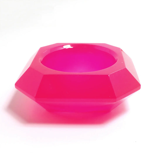Photo of the handmade resin geometric decorative pot. The resin is neon pink in color. It has a faceted octagon shape that tapers down to the bottom. There is a circular opening in the middle to put things.