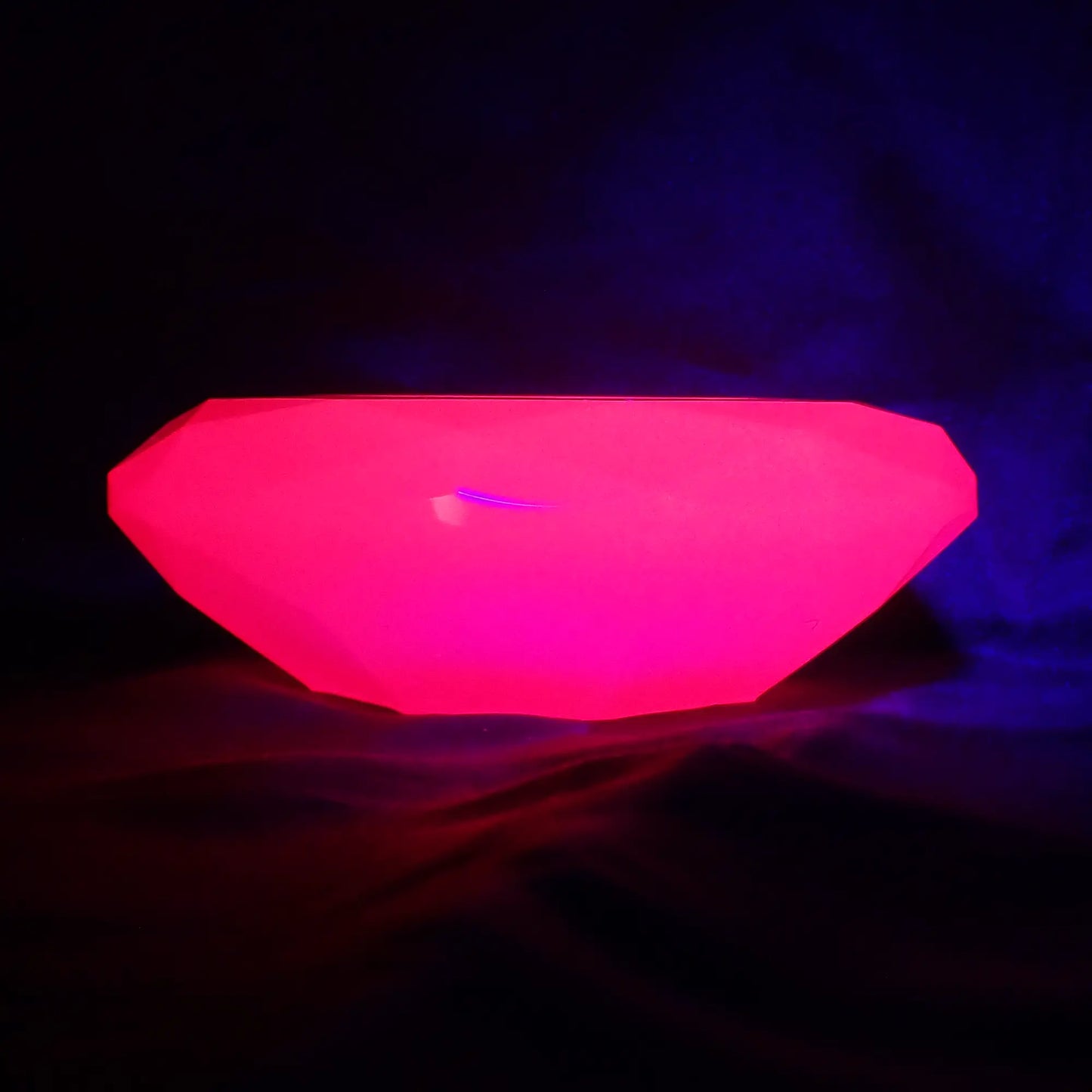 Photo of the handmade neon pink resin faceted round decorative pot fluorescing under a UV light.