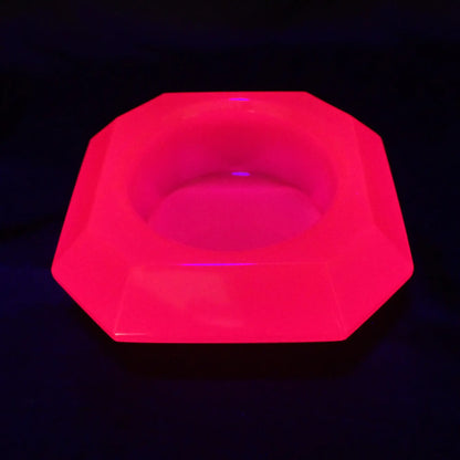 Photo of the handmade neon pink resin geometric octagon decorative pot fluorescing under a UV light.
