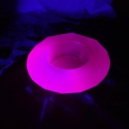 Photo of the handmade neon purple resin faceted round decorative pot fluorescing pink under a UV light.