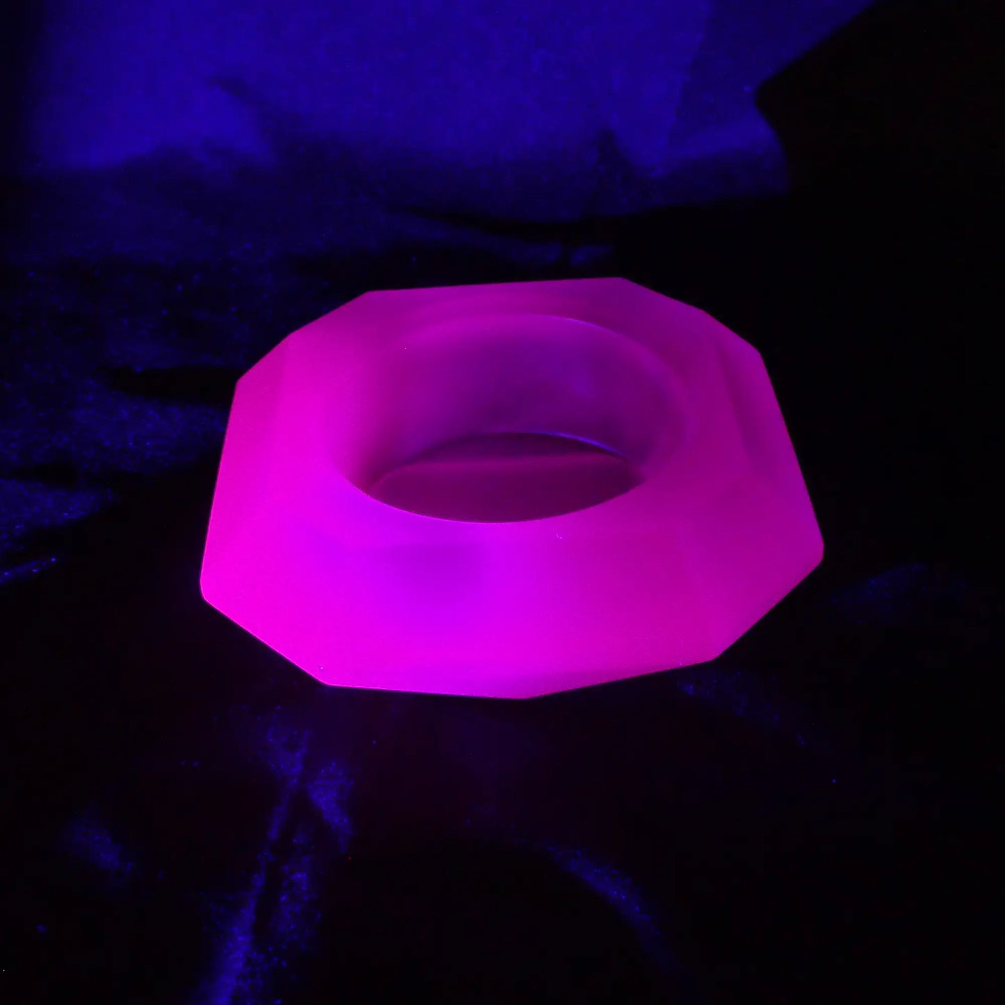 Photo of the handmade neon purple resin geometric octagon decorative pot fluorescing pink under a UV light.
