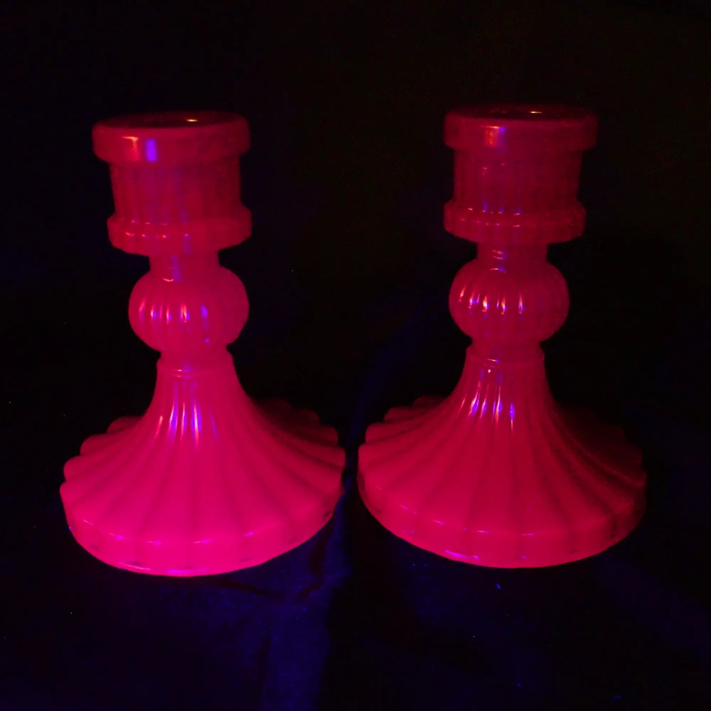 Photo of the vintage style handmade neon purple resin candlestick holders fluorescing pink under a UV light.