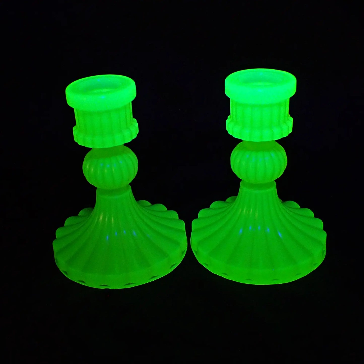 Photo of the neon yellow vintage style handmade resin candlestick holders fluorescing bright green under a UV light.