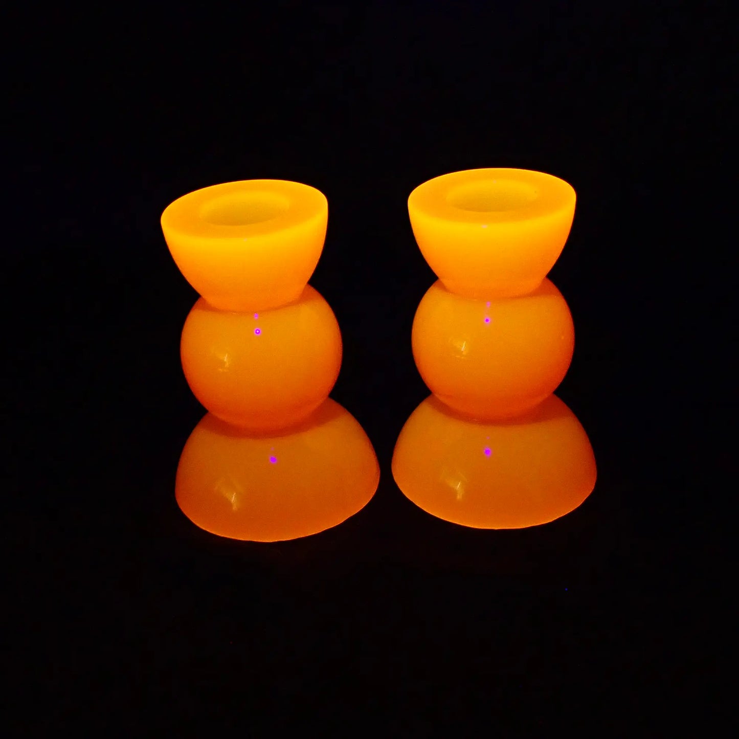 Photo showing how the handmade resin neon orange geometric candlestick holders fluoresce bright orange under a UV light.